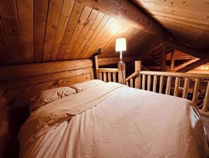 Une chambre dans une cabane en bois, avec un lit, une table de chevet et une lampe.