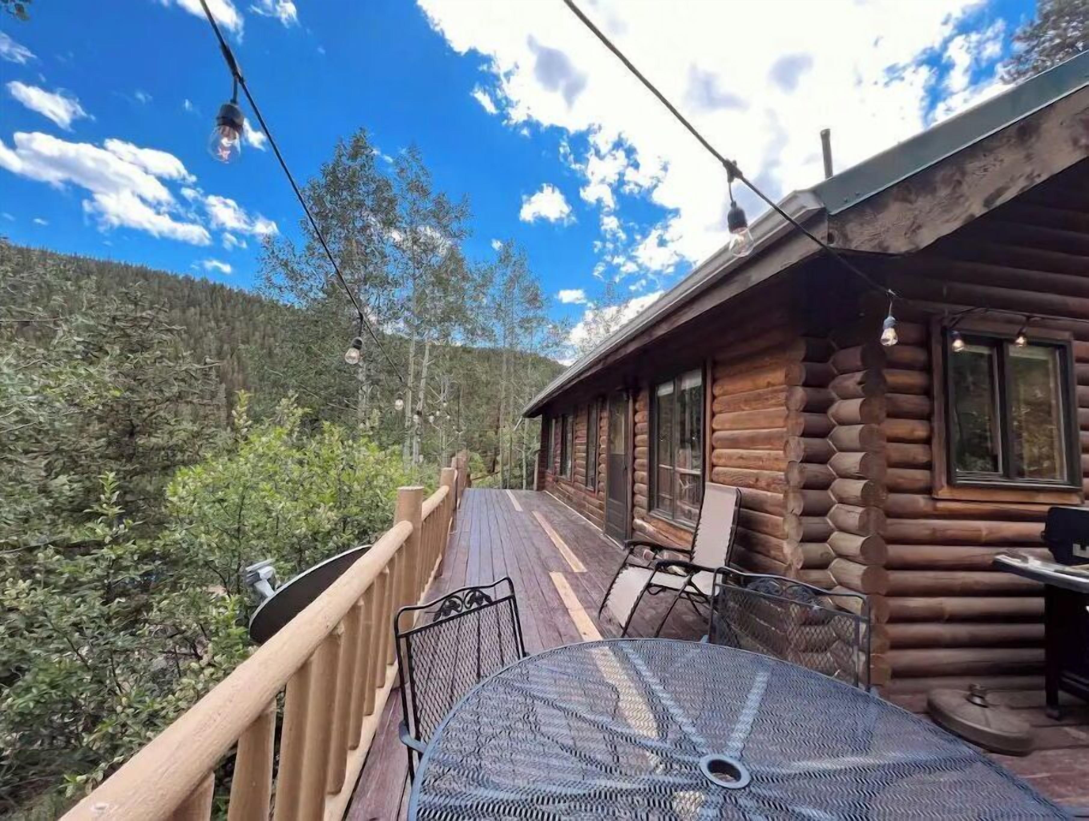 A wooden cabin with a deck, metal table, and chairs.