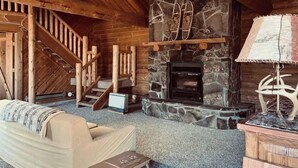 Interior acogedor de una cabaña con chimenea de piedra, escalera de madera y una zona de estar cómoda.