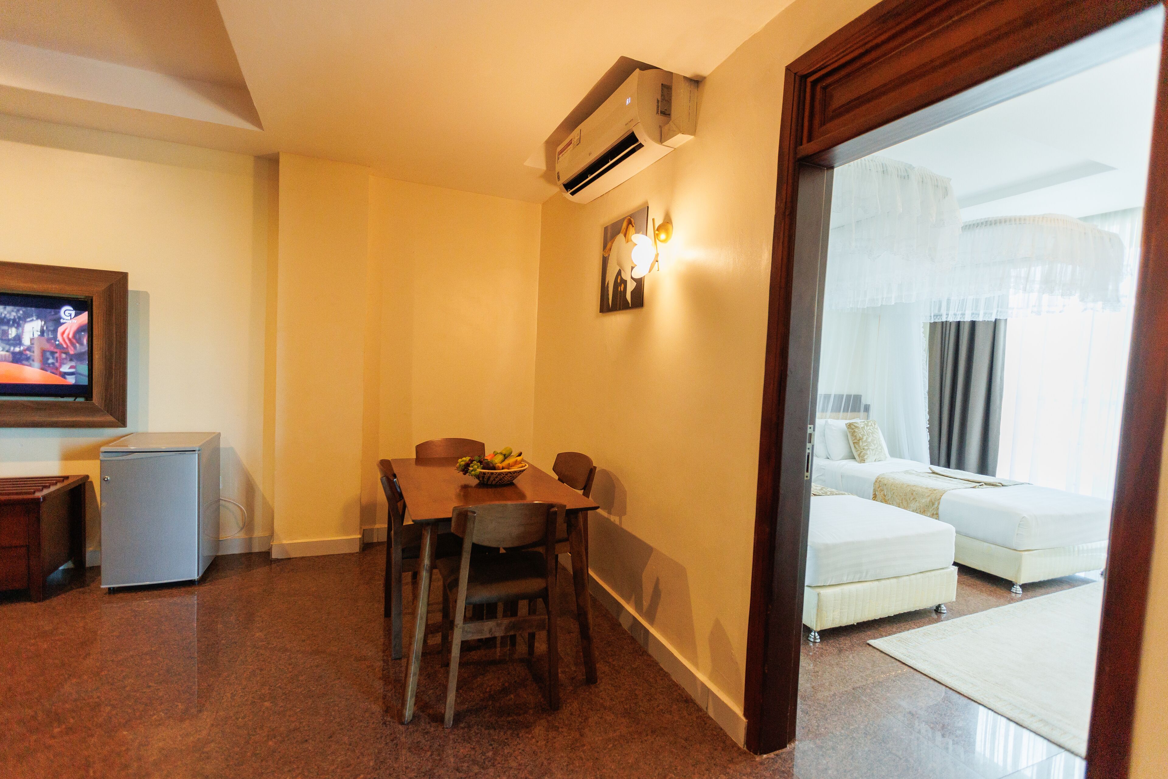 A hotel room with a dining area, a small refrigerator, a bed, and a television.