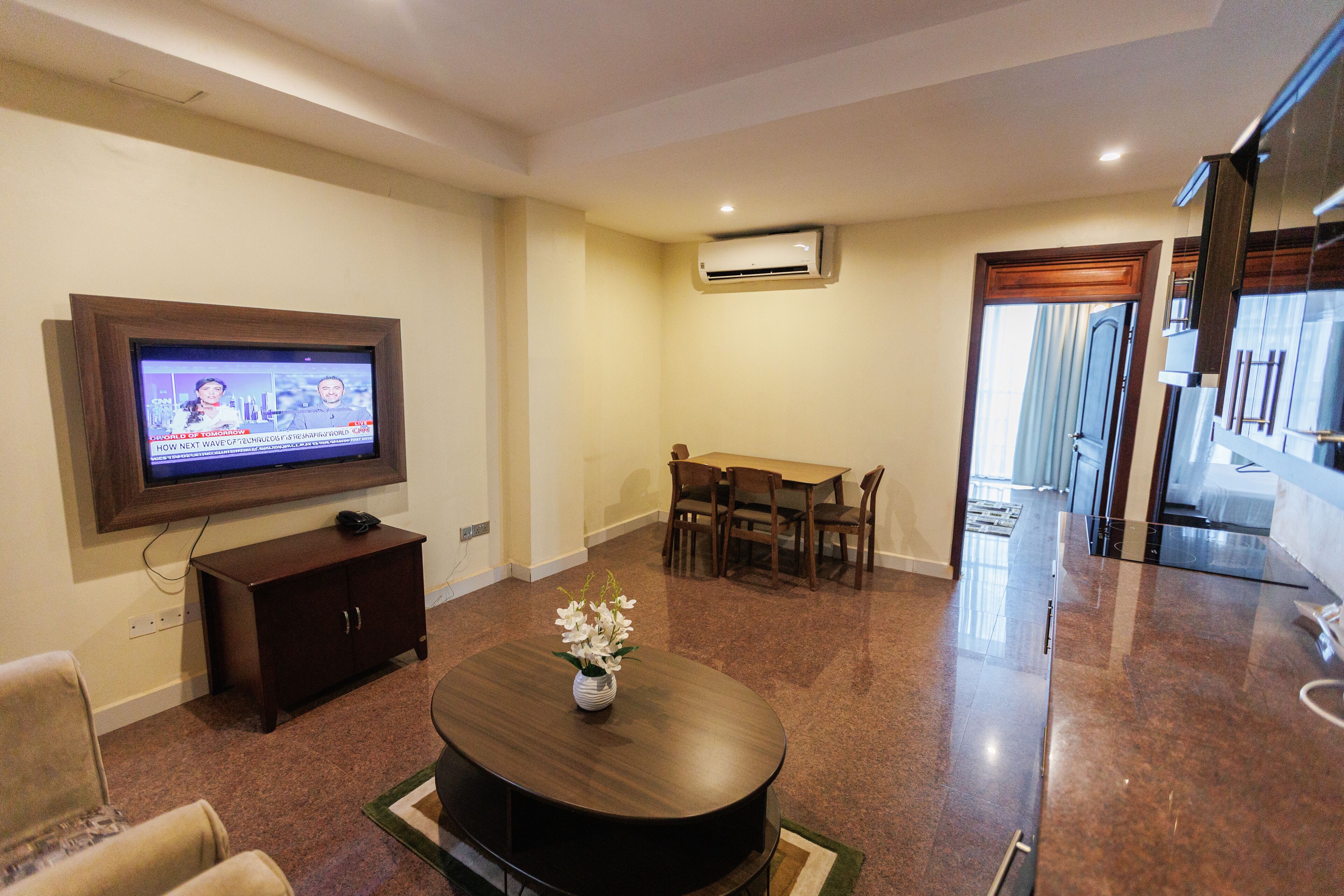 A living room with a flat-screen TV, a dining table, and a coffee table with a vase of flowers.