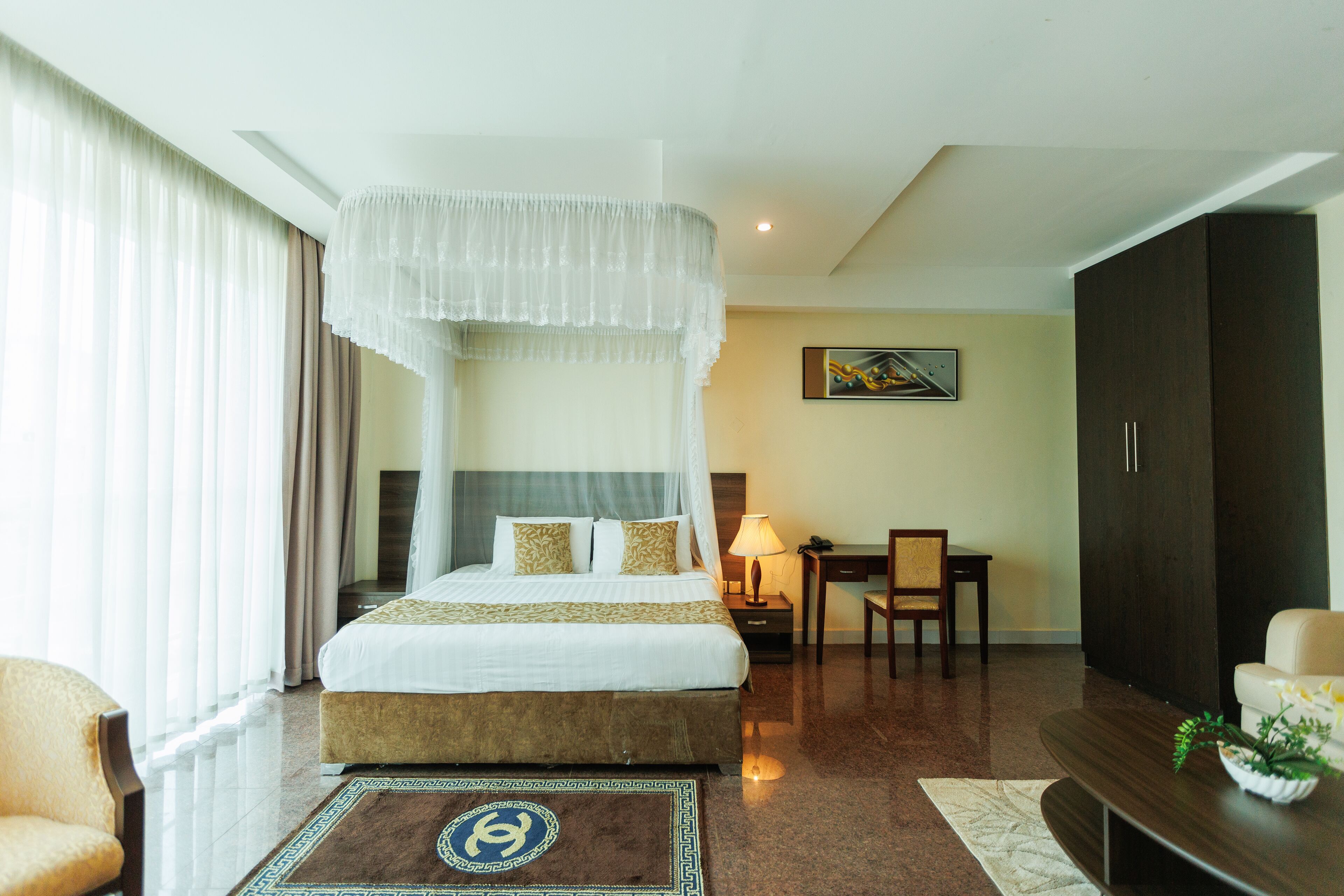 A hotel room with a four-poster bed, a desk with a chair, a television, and a large wardrobe.