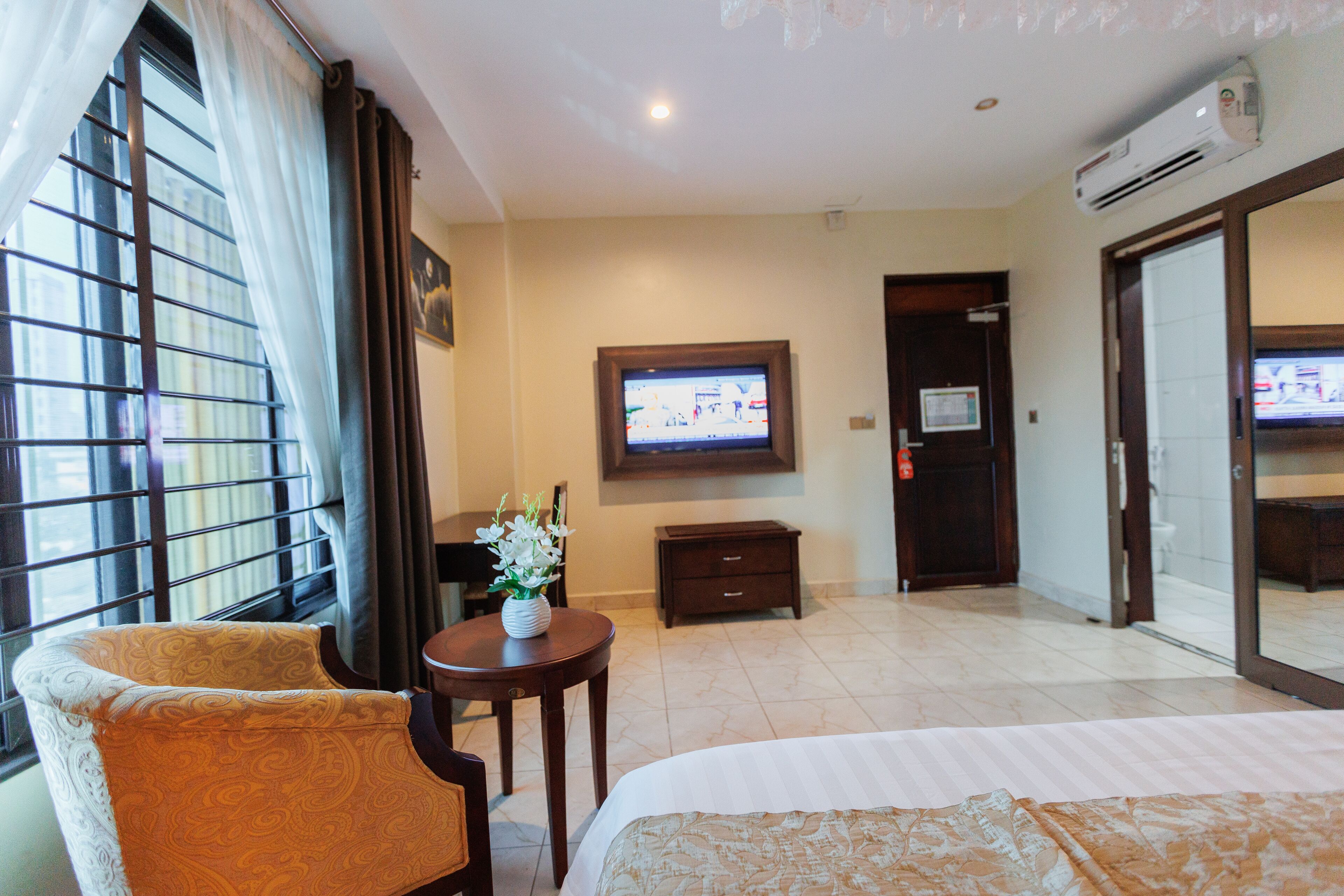Habitación de hotel con cama, una silla, una mesita con un florero, televisión y una puerta corredera que da a un baño.