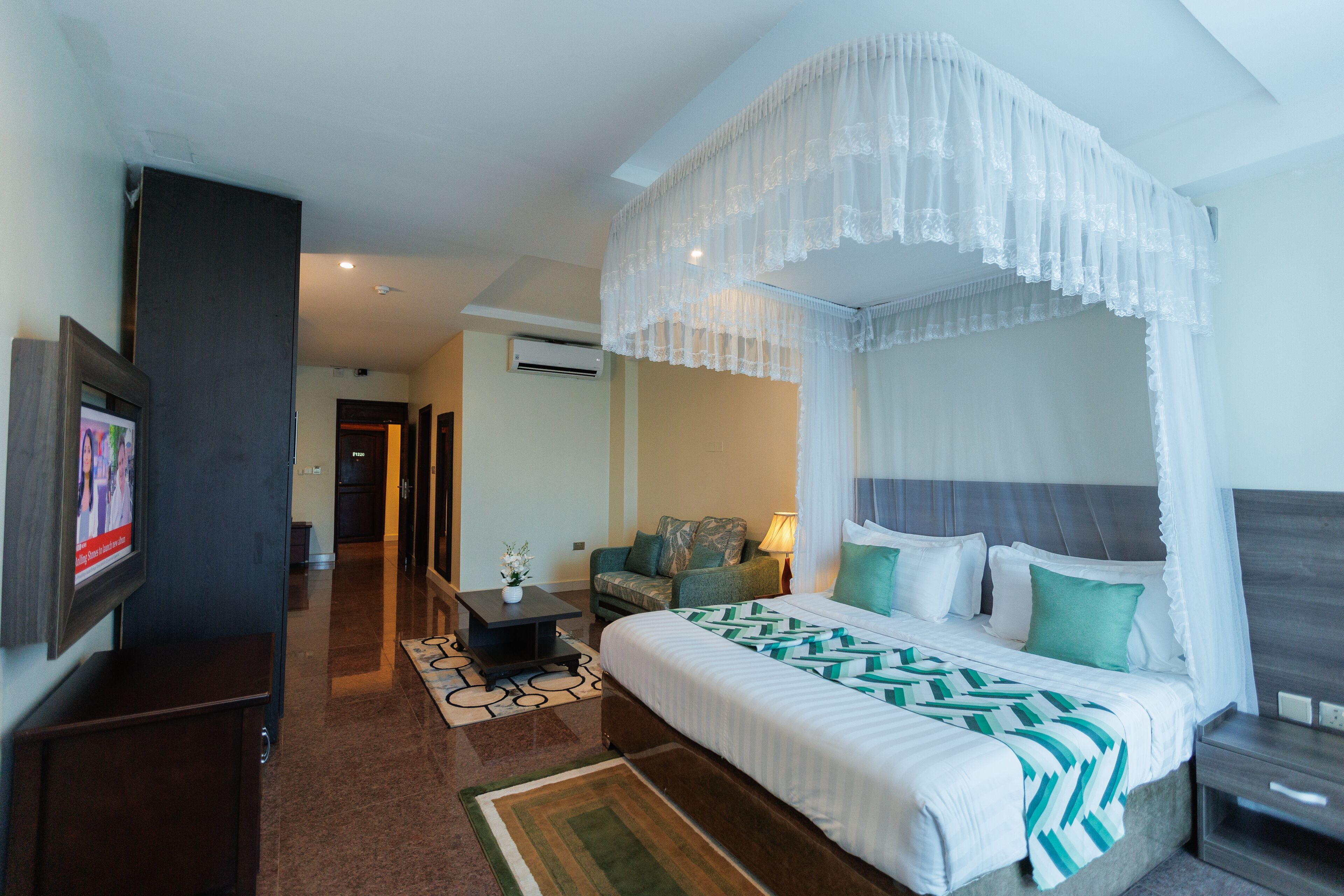 A hotel room with a four-poster bed, a television, a desk, and a sofa.