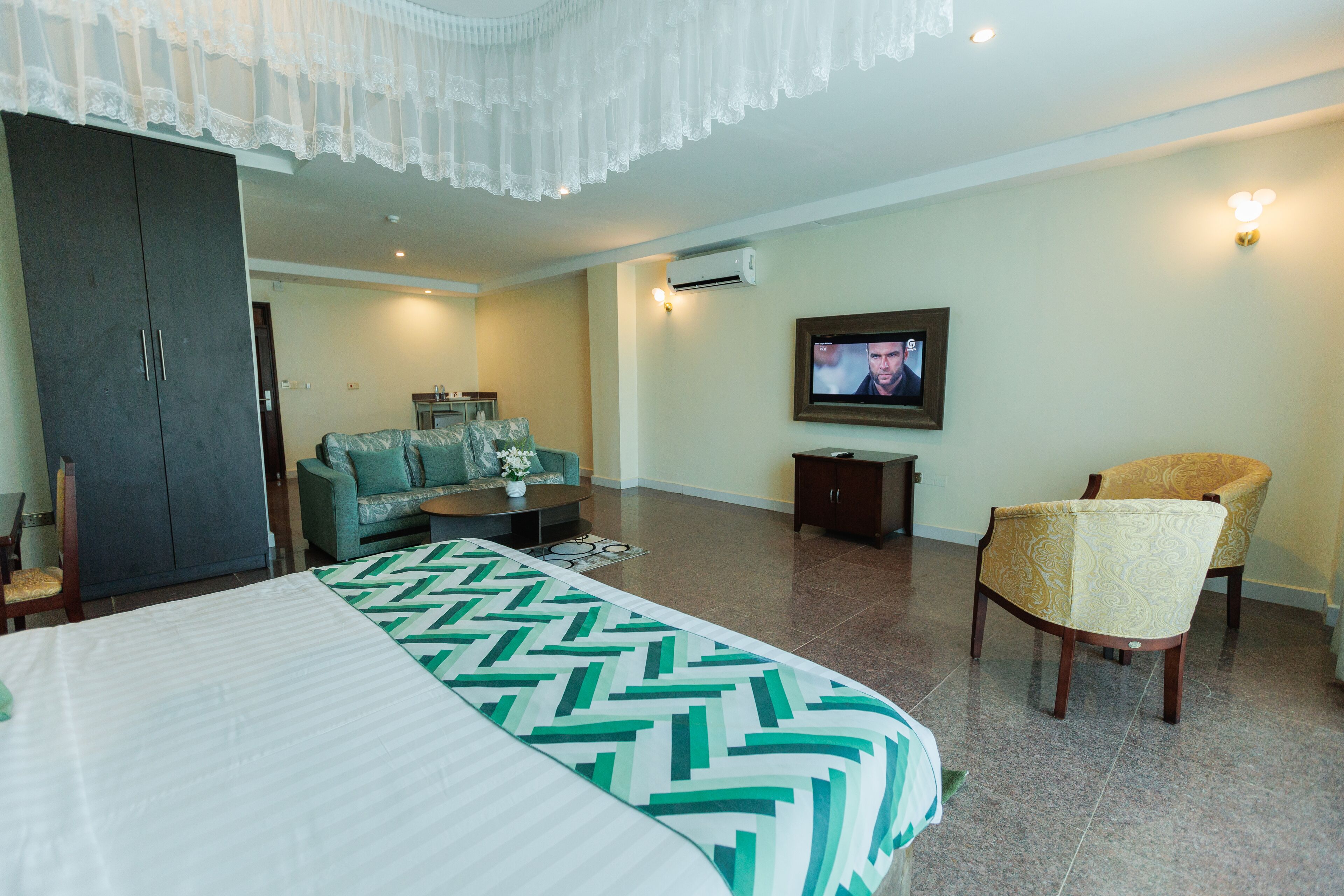 A hotel room with a bed, a sofa, a chair, a television, and a wardrobe.