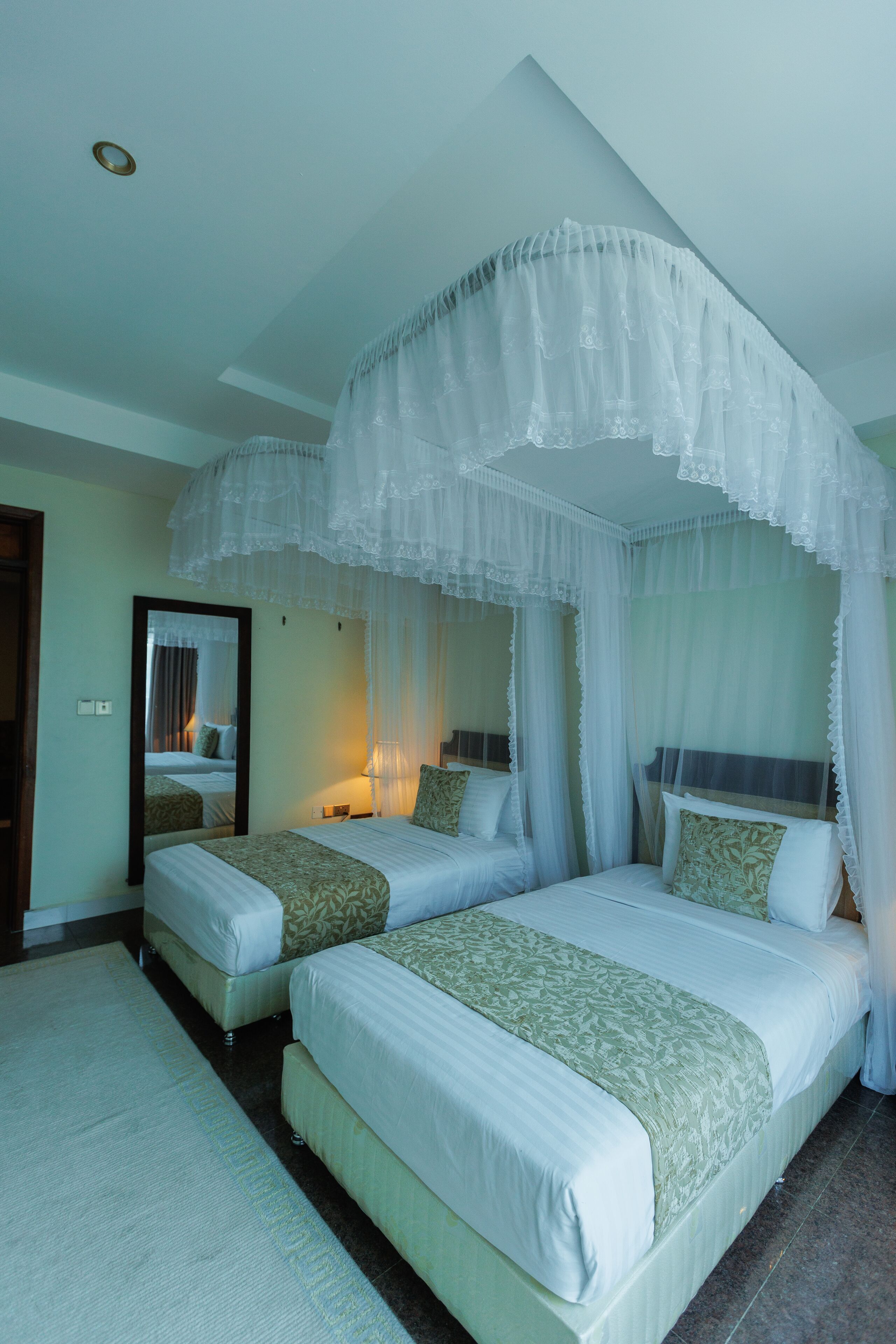 A hotel room with two beds, a canopy bed, a mirror, and a nightstand with a lamp.