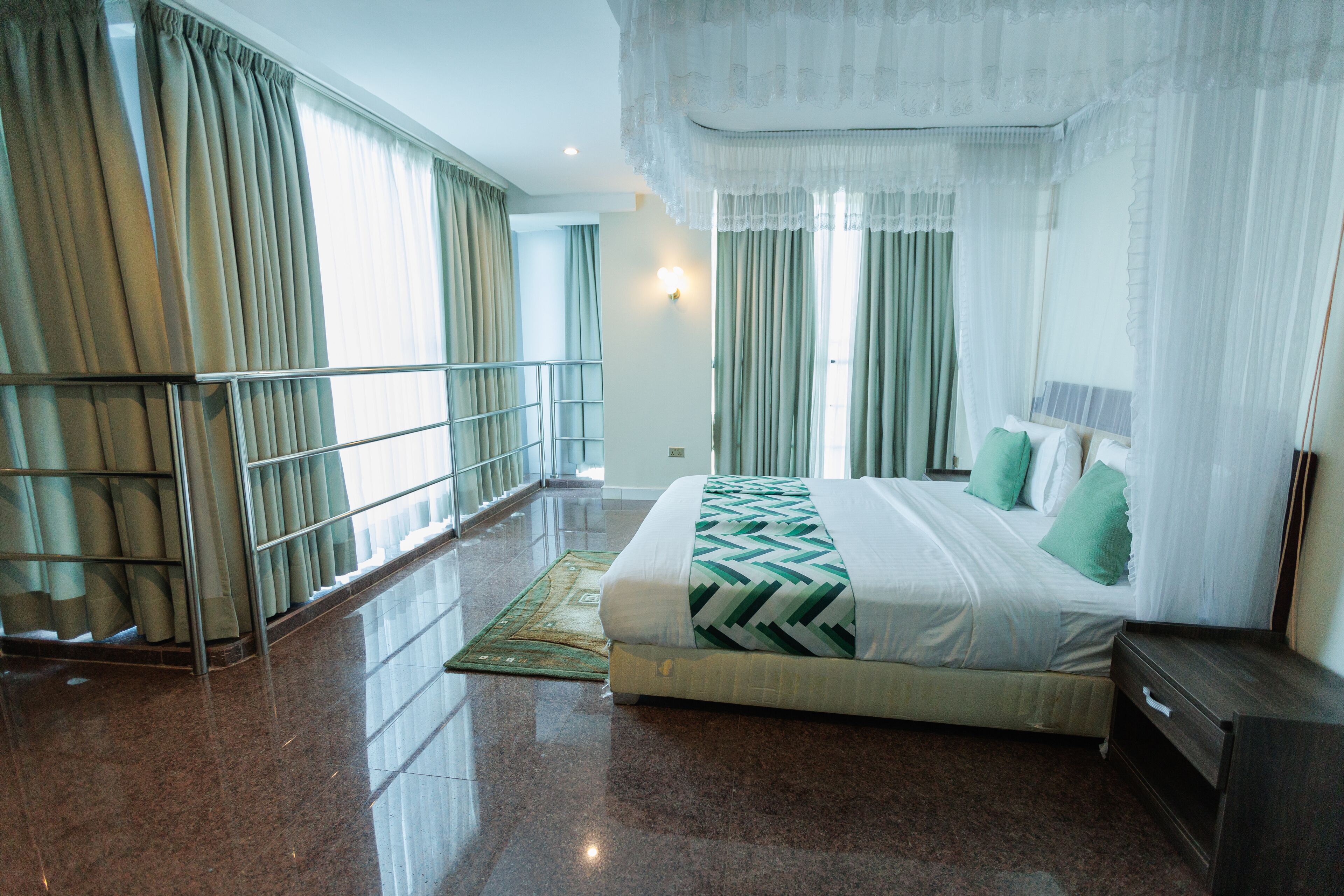 A hotel room with a large bed, a nightstand, a window with curtains, and a view of the outside.