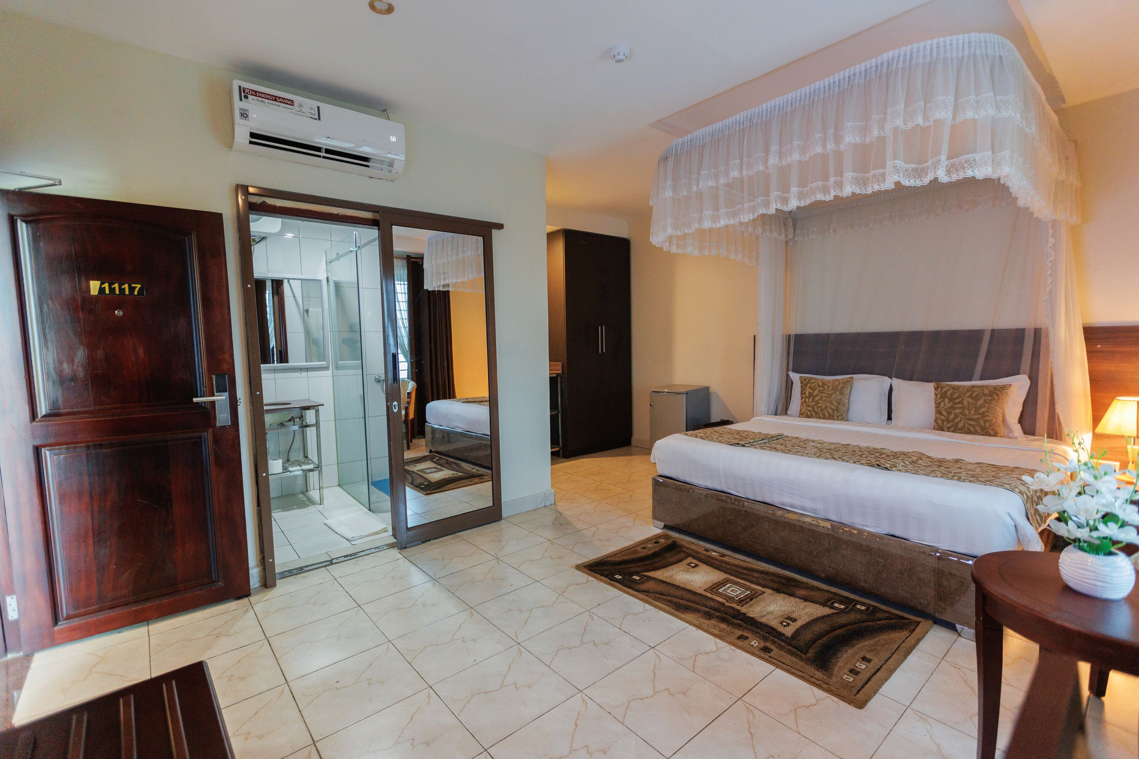 A hotel room with a large bed, a wardrobe, a mirror, and a small table with a vase of flowers.
