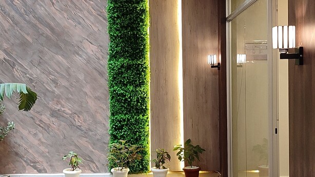 Un hall d’entrée moderne avec un sol en marbre, un jardin vertical et une porte en verre.