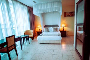 Una habitación de hotel con una cama, dos mesitas de noche con lámparas, una silla, un escritorio y un espejo grande.