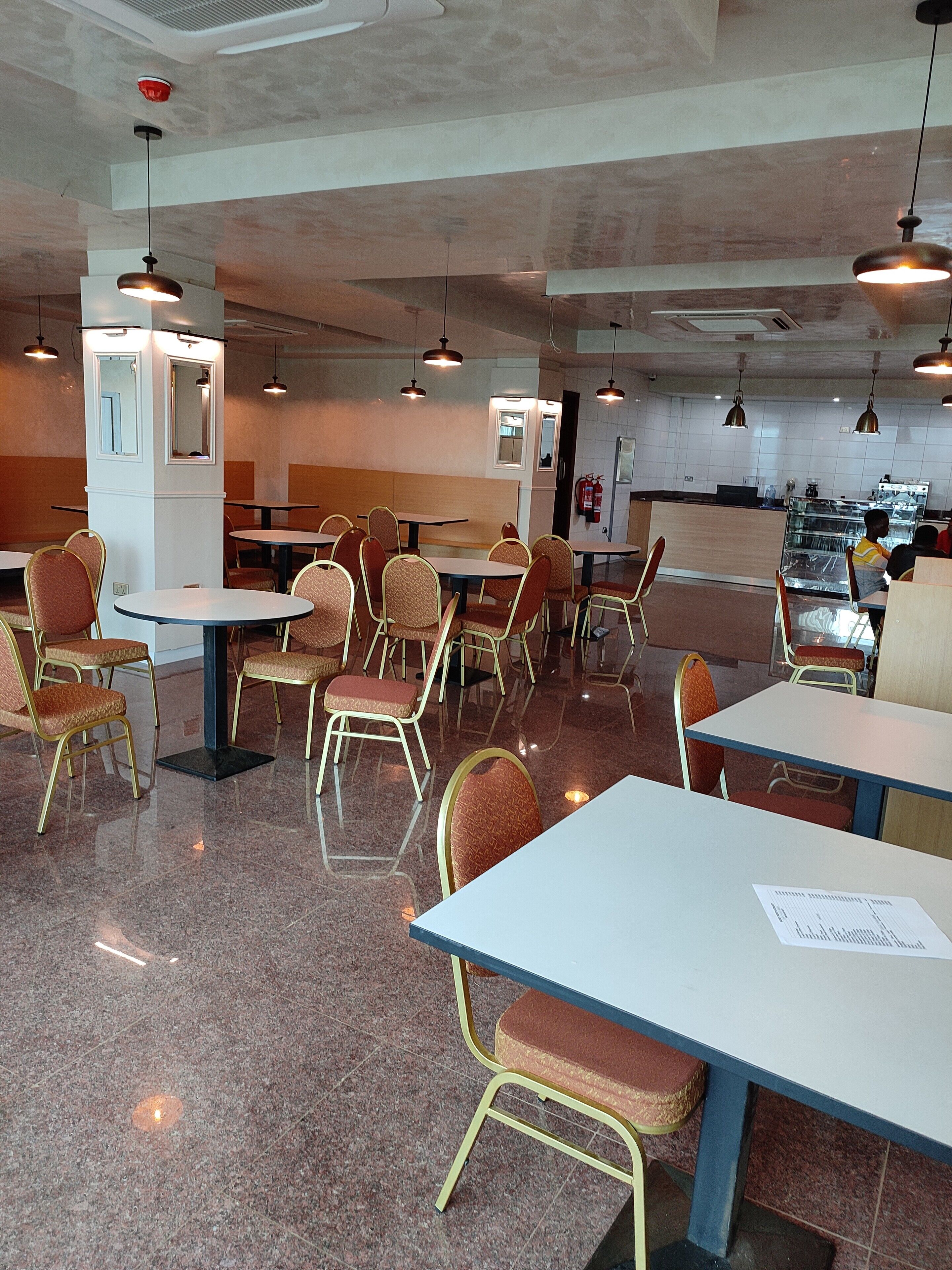 Un restaurante con varias mesas y sillas, una zona de cocina y un extintor en la pared.