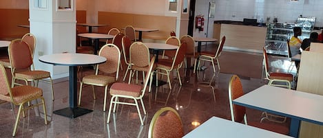 A restaurant with multiple tables and chairs, a kitchen area, and a fire extinguisher on the wall.