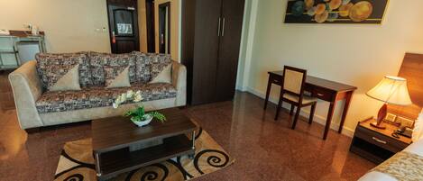 A hotel room with a sofa, a coffee table, a desk, a chair, a lamp, and a bed.