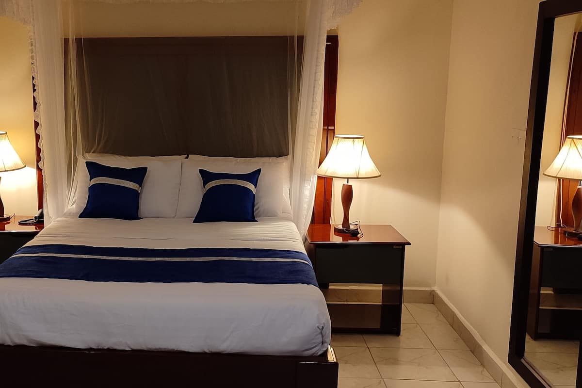 Una cama cuidadosamente hecha con dosel, dos lámparas de noche y un espejo en la pared.