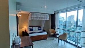 Une chambre d’hôtel équipée d’un lit, d’une table de chevet, d’une lampe et offrant une vue sur la ville grâce à de grandes fenêtres.