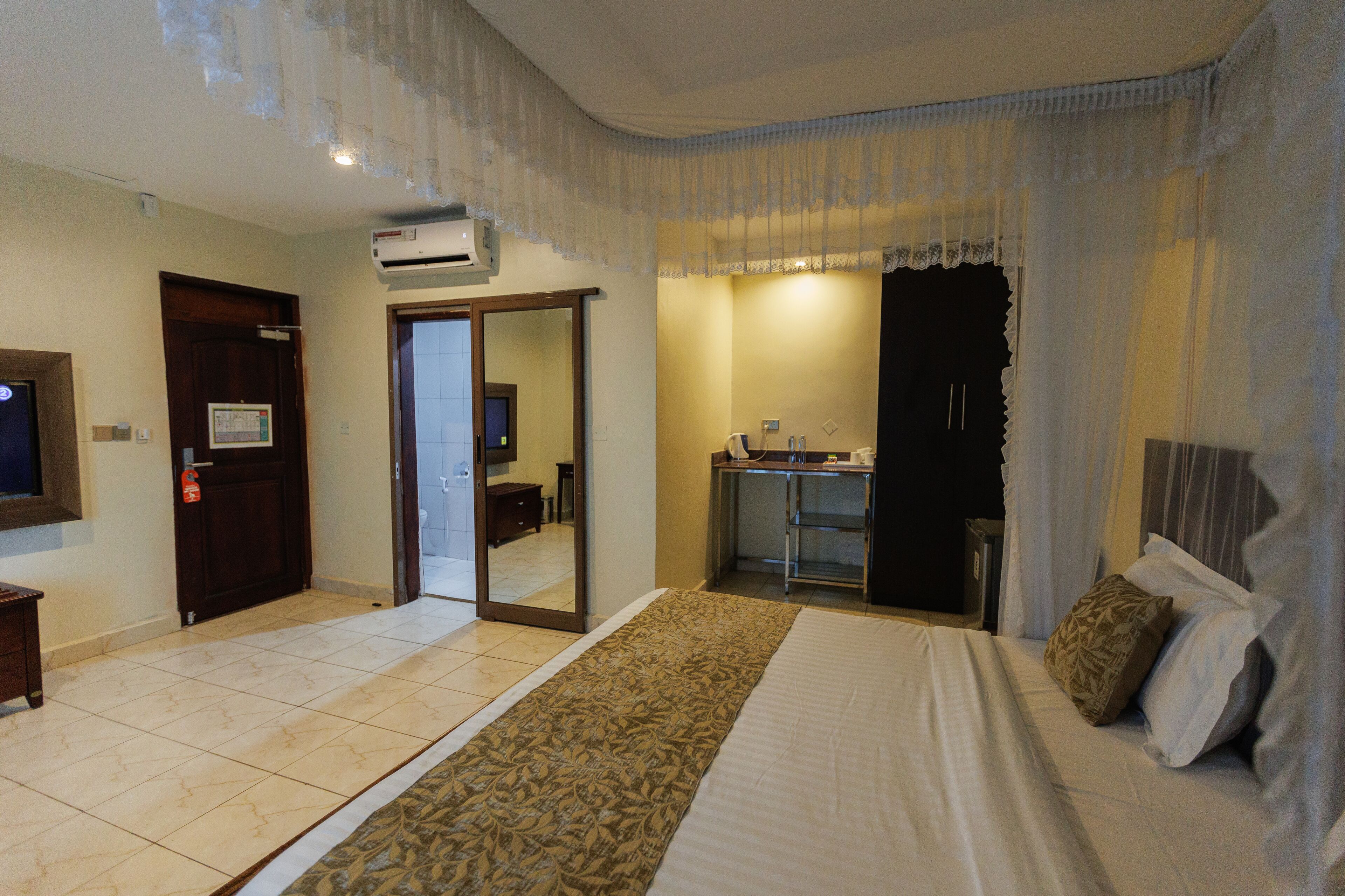 Habitación de hotel con una cama grande, un escritorio pequeño, un espejo y un baño visible a través de una puerta abierta.