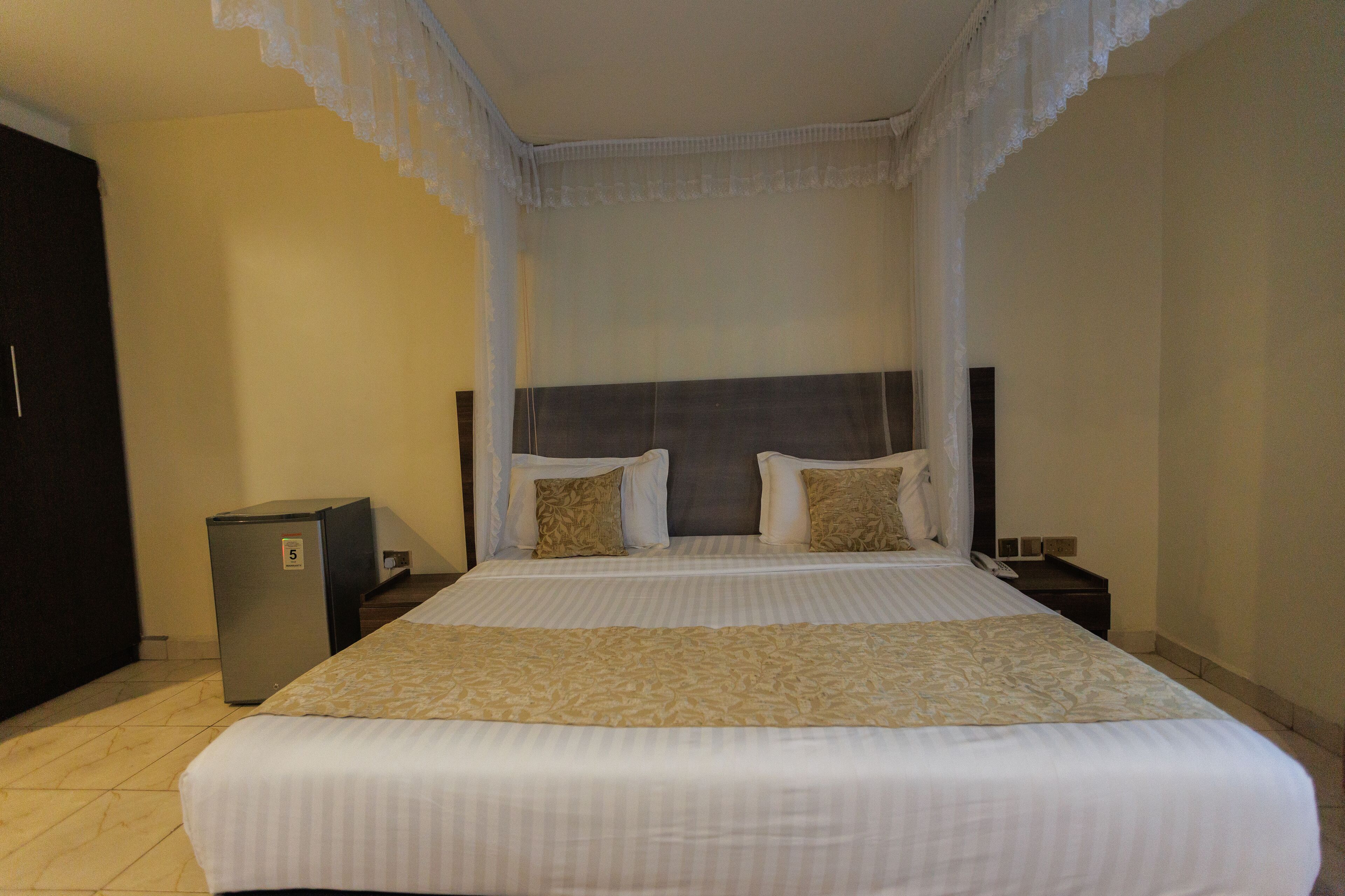 Una camera d'albergo con un letto grande, un comodino, un piccolo frigorifero e un armadio.