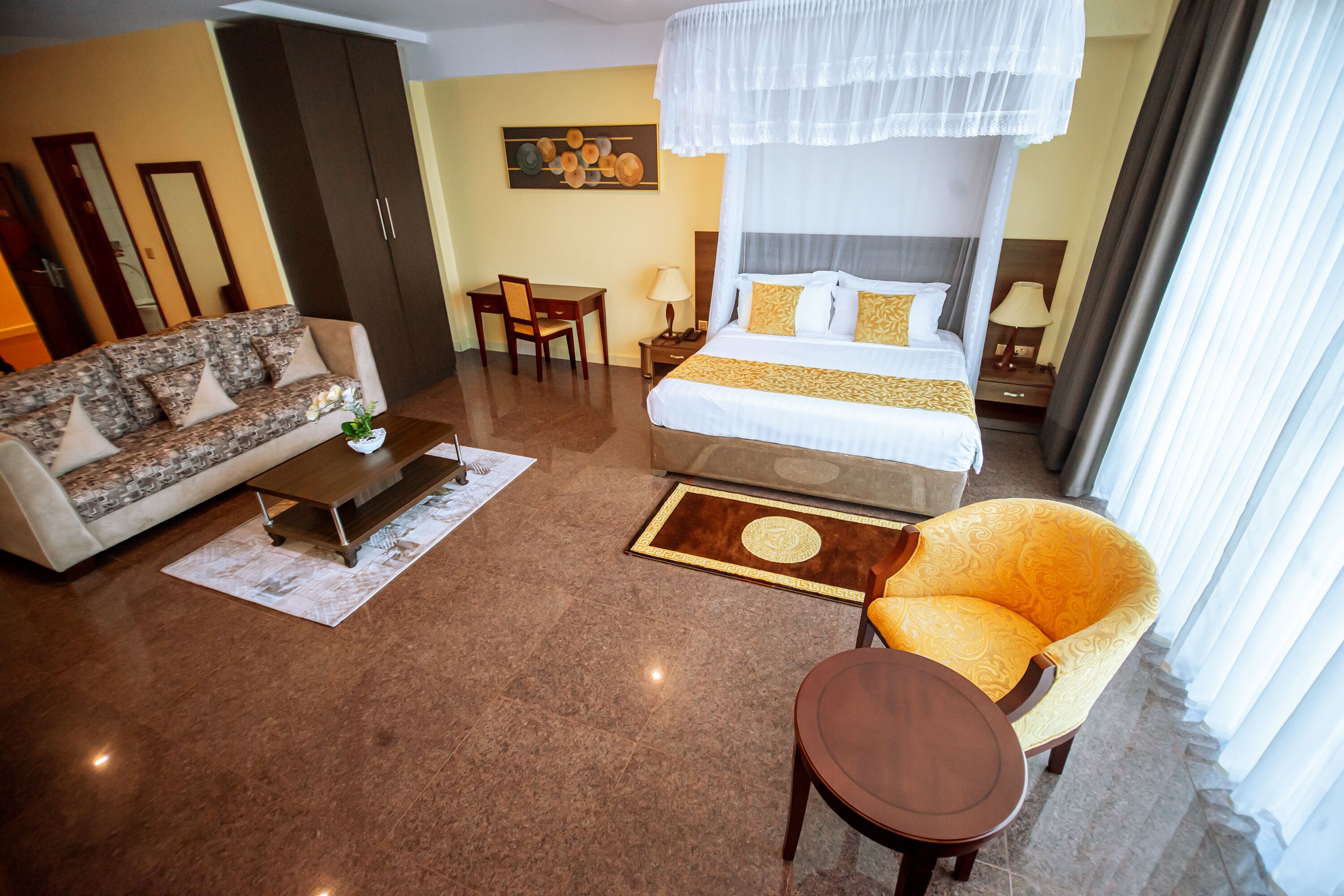 A hotel room with a large bed, a sofa, a chair, a small table, and a nightstand.