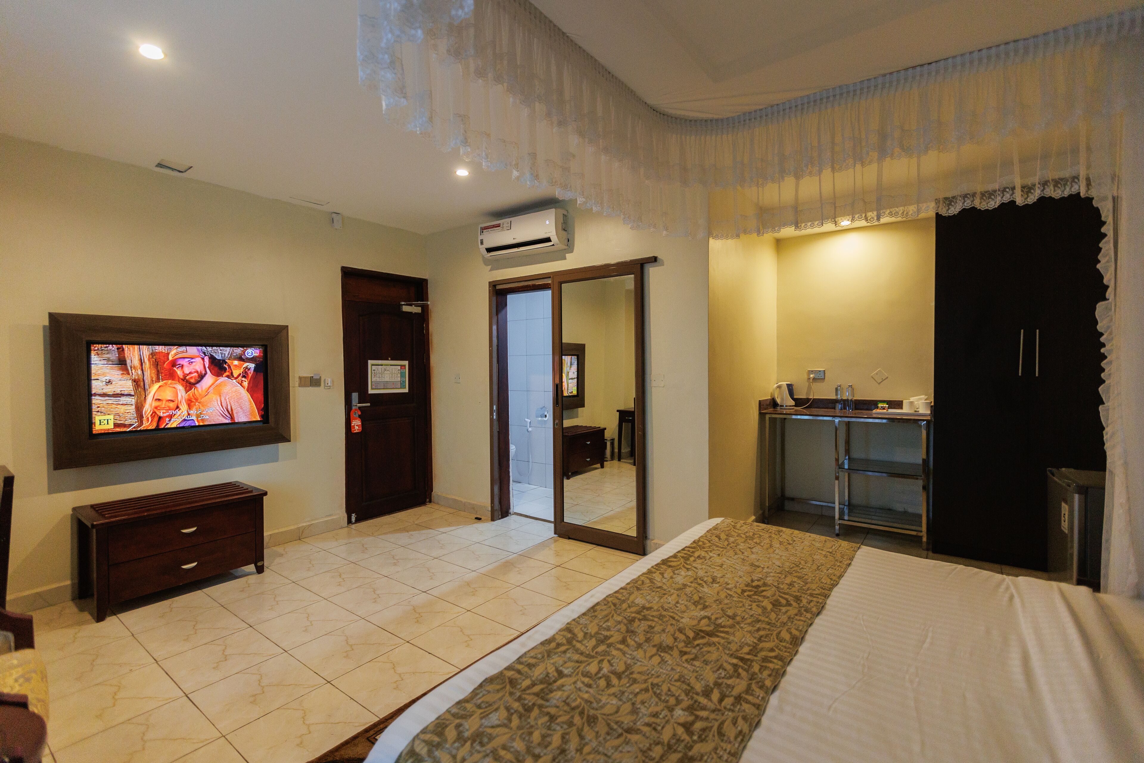 A hotel room with a bed, a television, a wardrobe, a mirror, and a kitchenette.