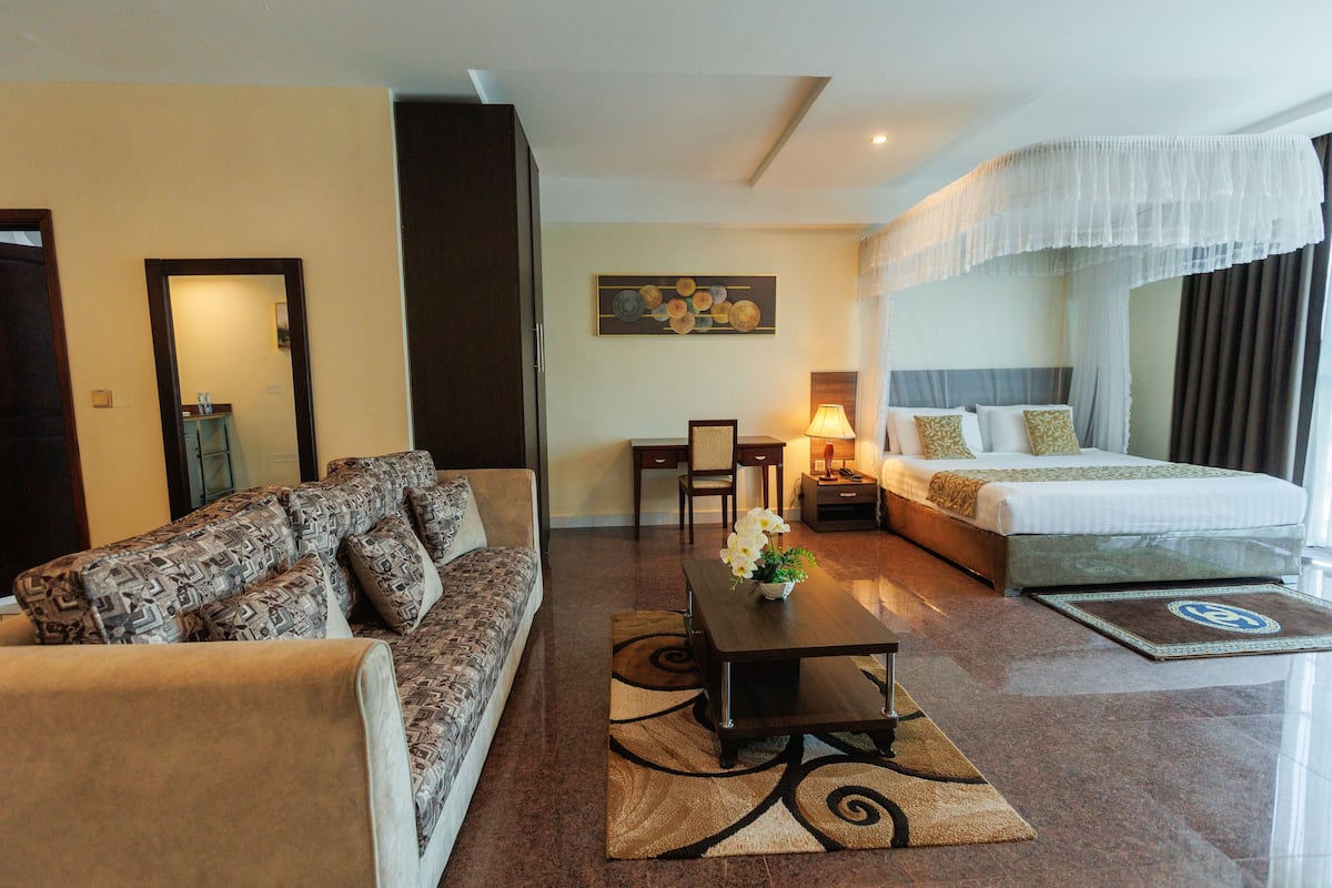 Habitación de hotel con sofá, mesa de centro, cama con dosel, un cuadro en la pared y una alfombra.