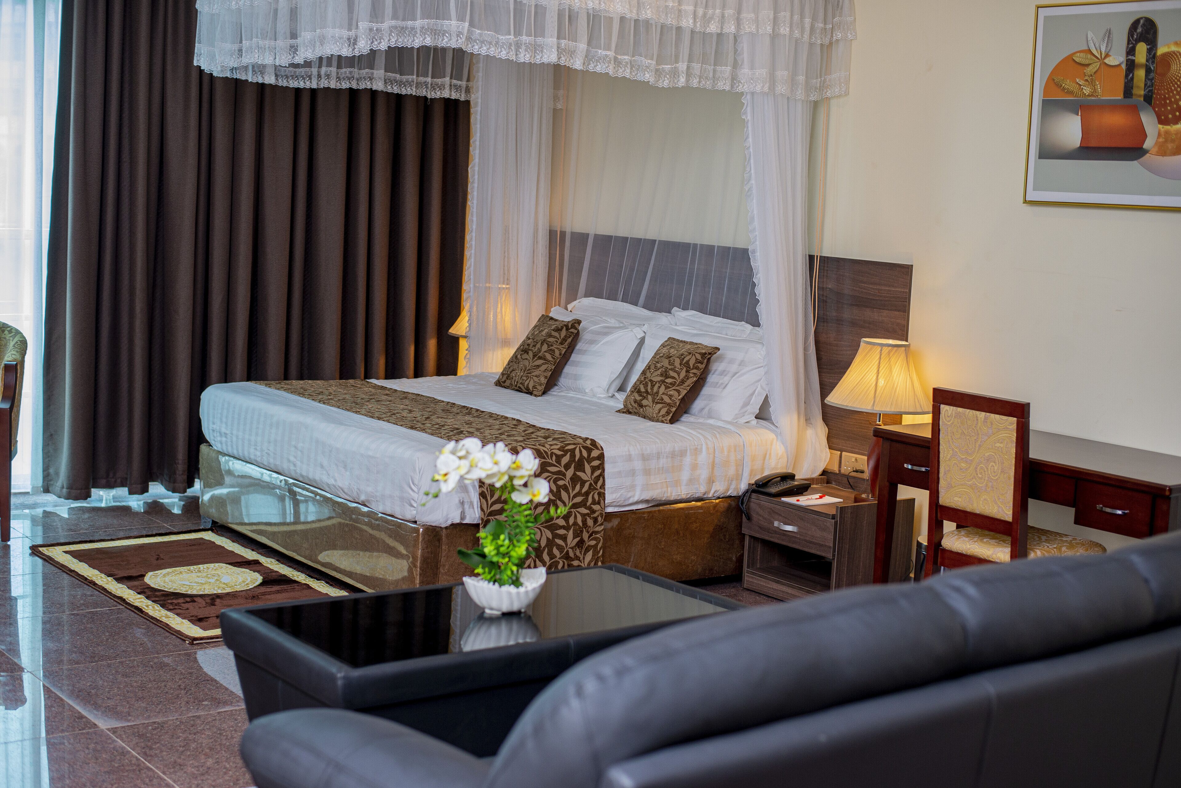 Una habitación de hotel con cama, mesita de noche, lámpara, silla y un florero con flores.