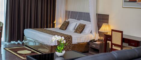 Una habitación de hotel con cama, mesita de noche, lámpara, silla y un florero con flores.
