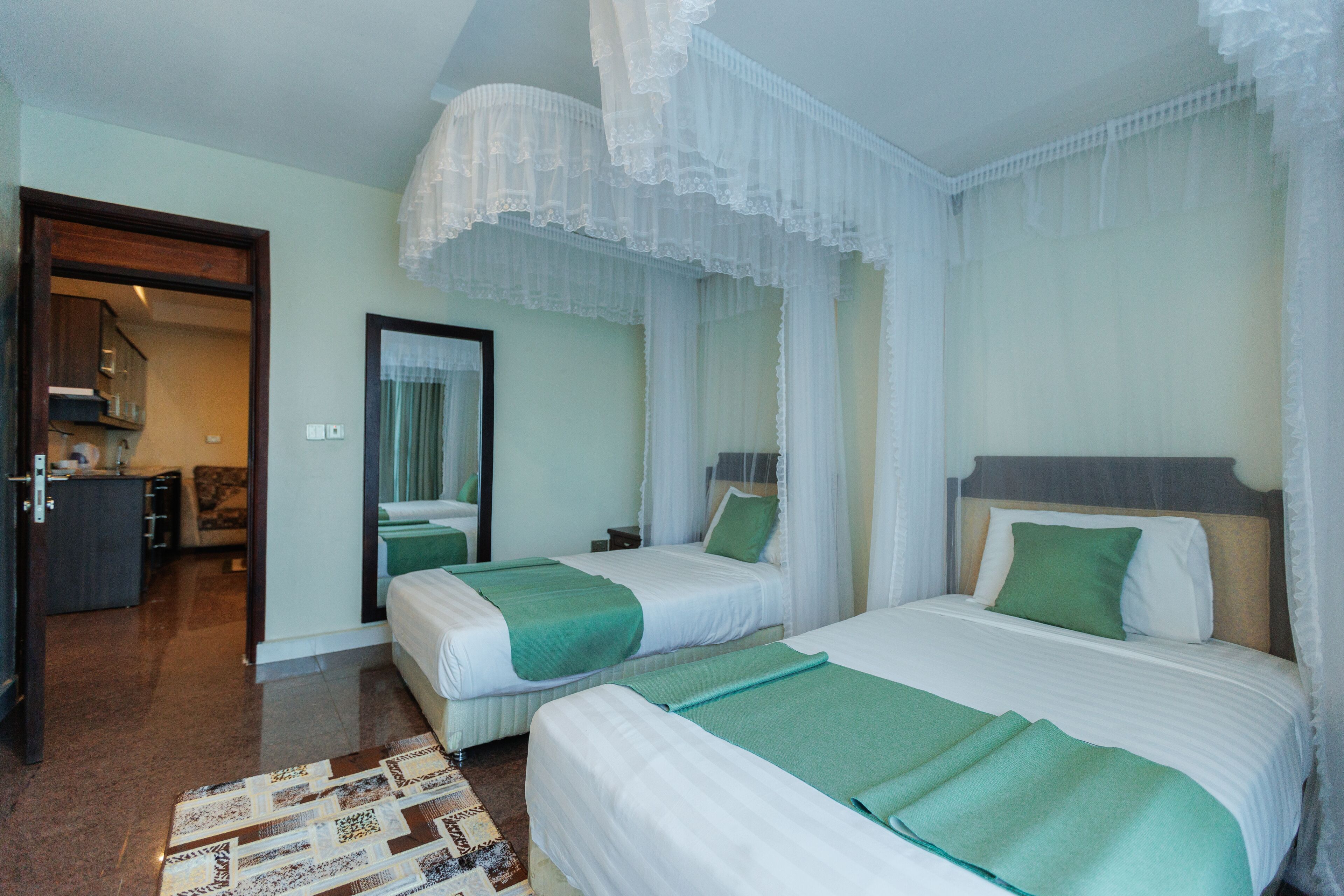 A hotel room with two beds, a bathroom, and a kitchenette.