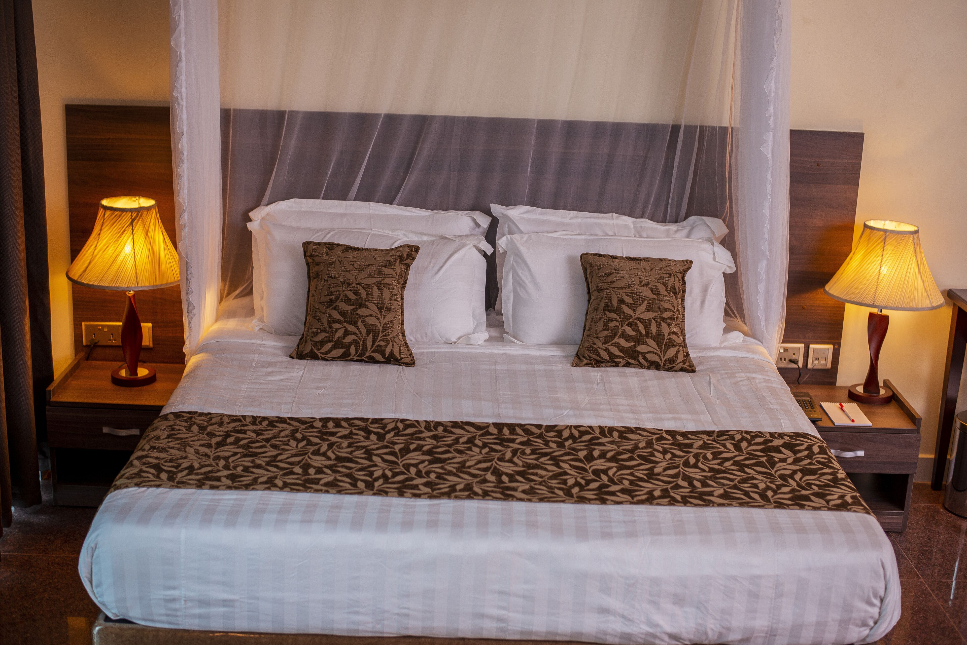 Un letto ben rifatto con tenda, due abat-jour e una coperta decorata.