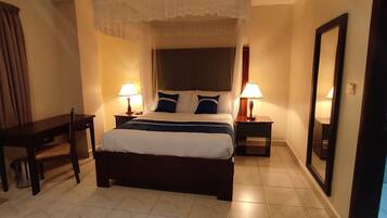 Une chambre d’hôtel comprenant un lit, deux tables de chevet avec des lampes, une chaise, un bureau et un grand miroir.