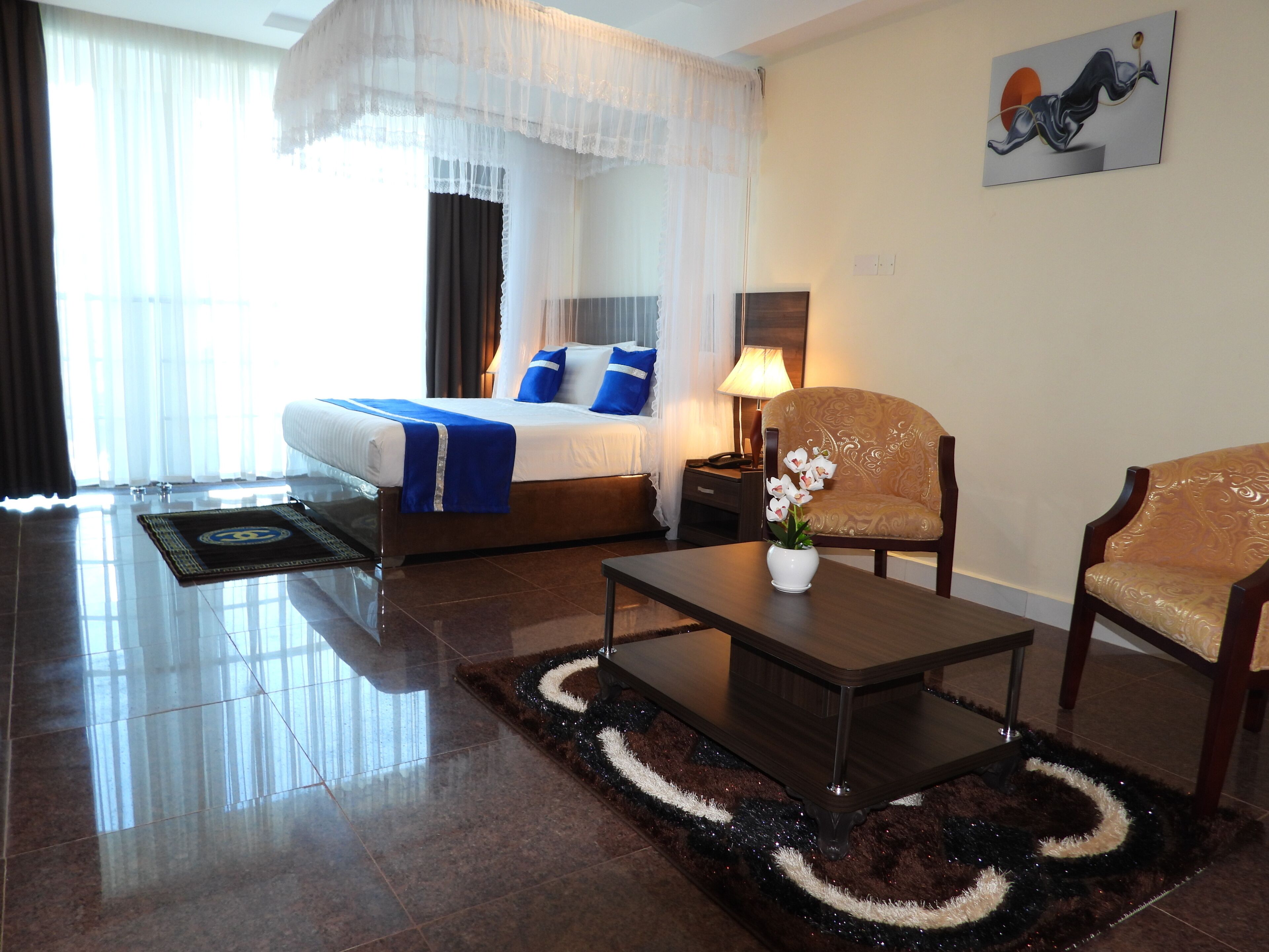 A hotel room with a bed, a nightstand, a lamp, two chairs, a coffee table, and a decorative rug.