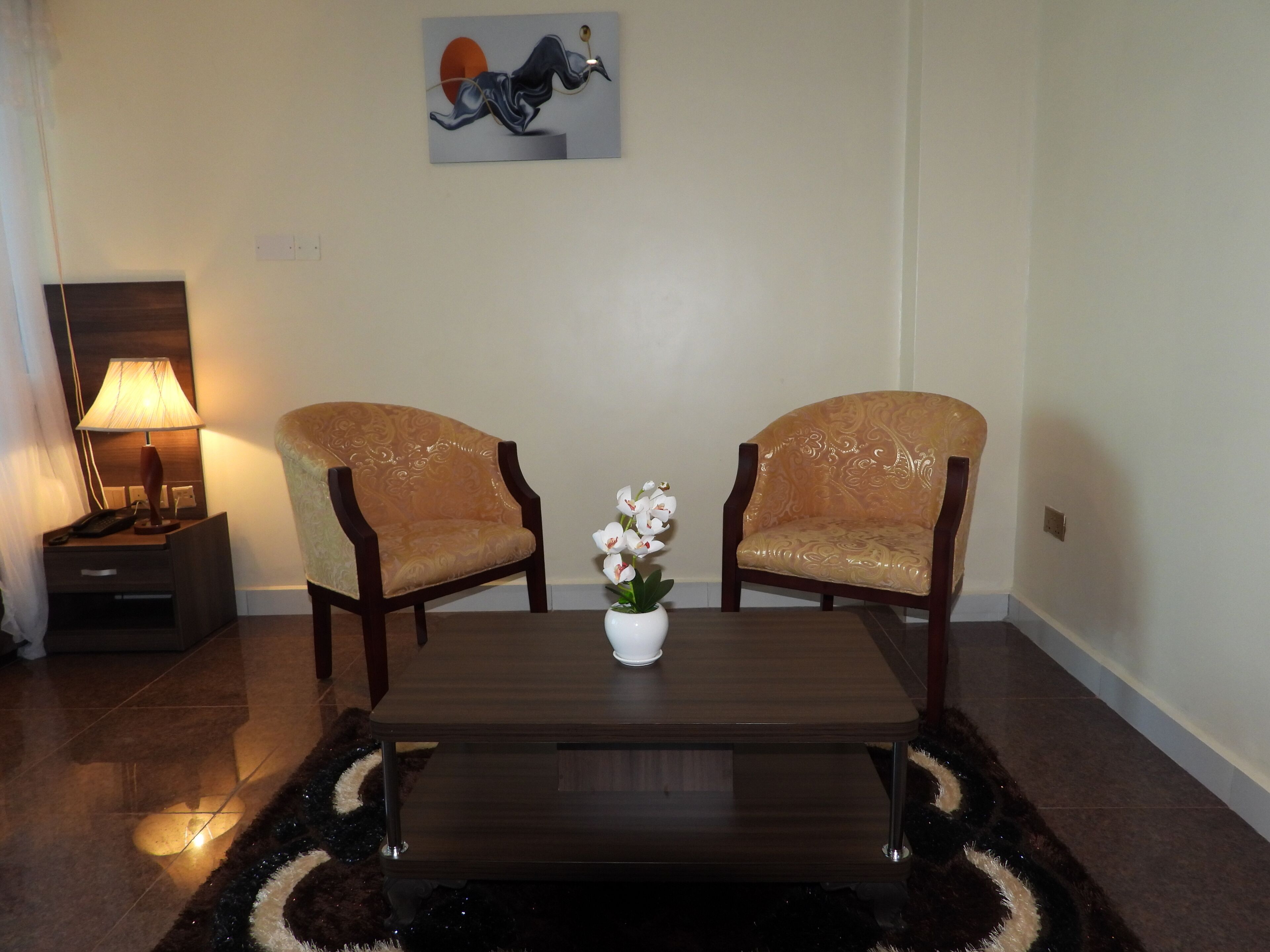 A room with two upholstered chairs, a coffee table, a lamp, and a vase with flowers.