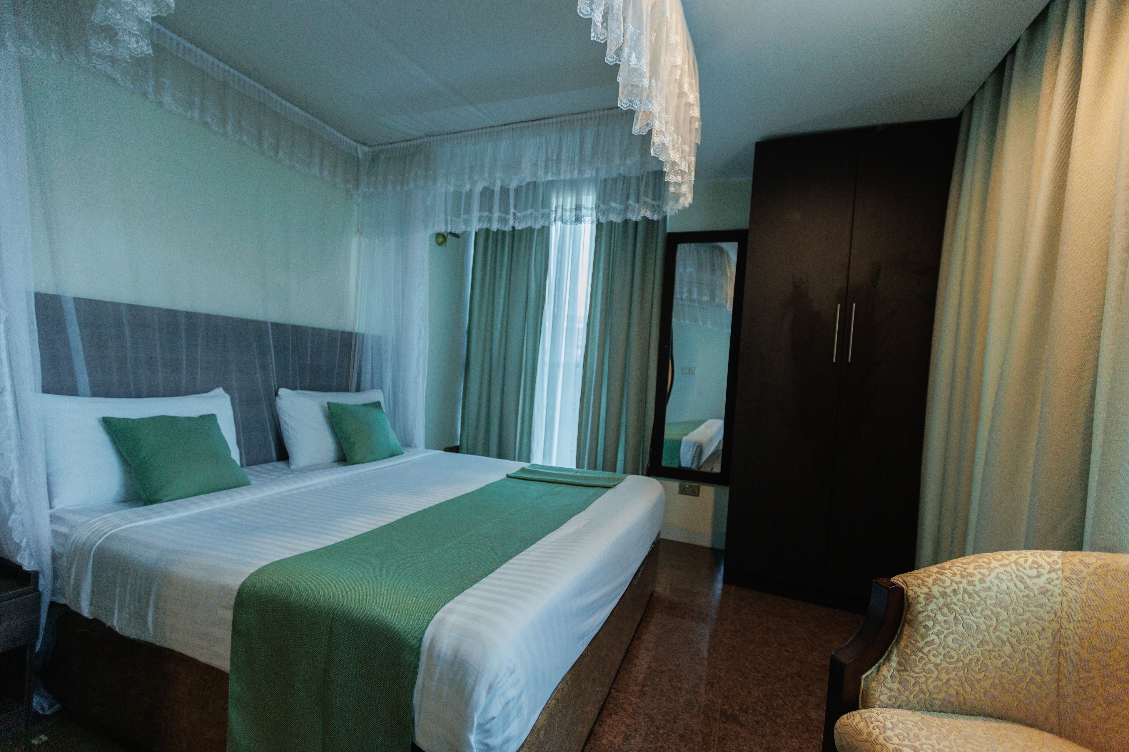 A hotel room with a large bed, a chair, a wardrobe, and a mirror.
