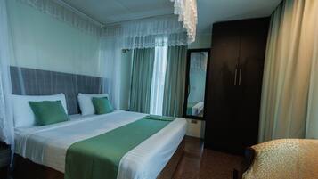 A hotel room with a large bed, a chair, a wardrobe, and a mirror.