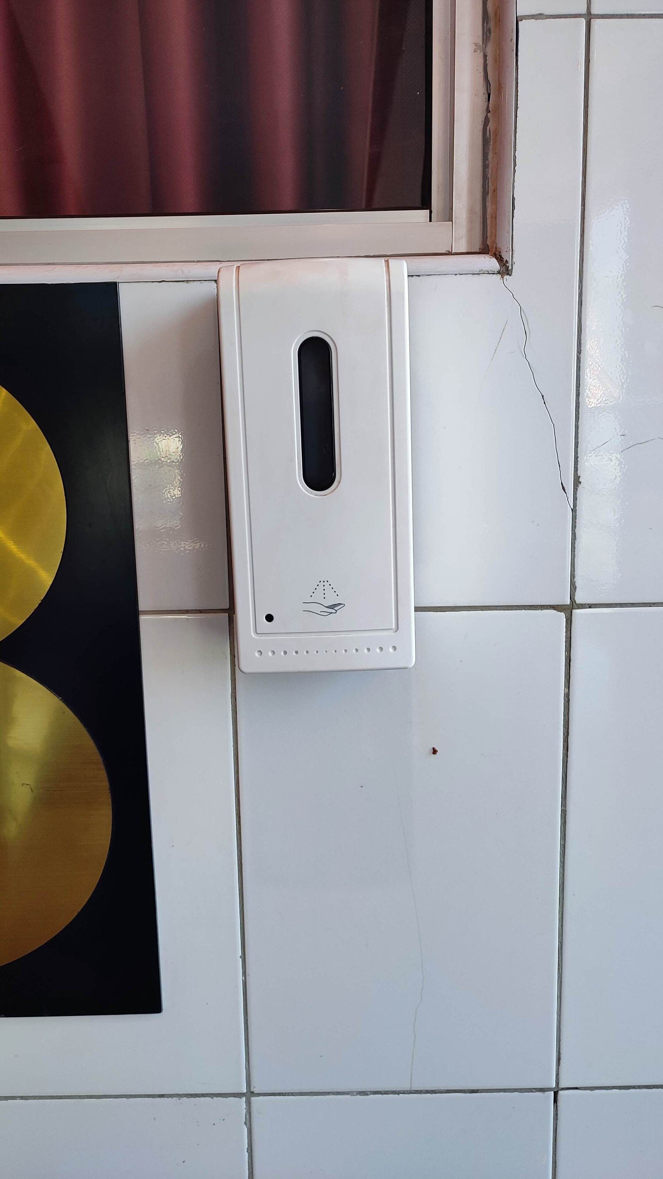 A hand sanitizer dispenser mounted on a tiled wall.