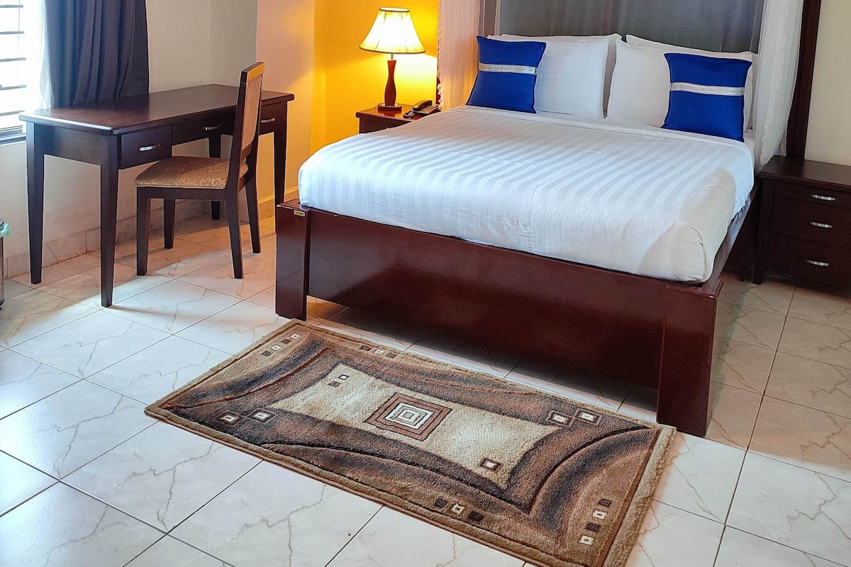 Una habitación de hotel con cama, escritorio, silla, lámpara y alfombra.