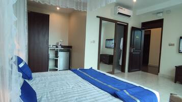 A hotel room with a bed, a wardrobe, a desk with a chair, a television, and an air conditioning unit.