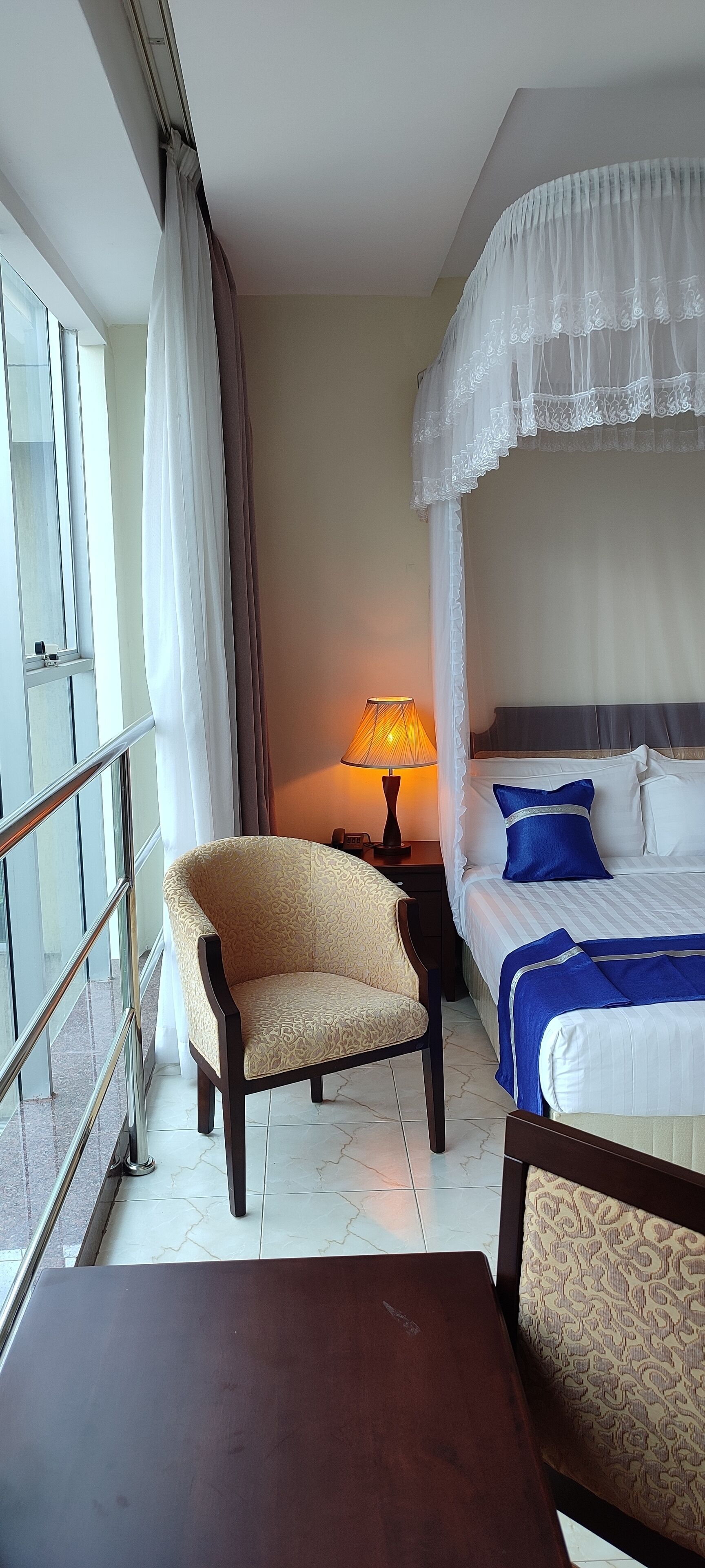 A hotel room with a bed, a chair, a table, and a lamp.