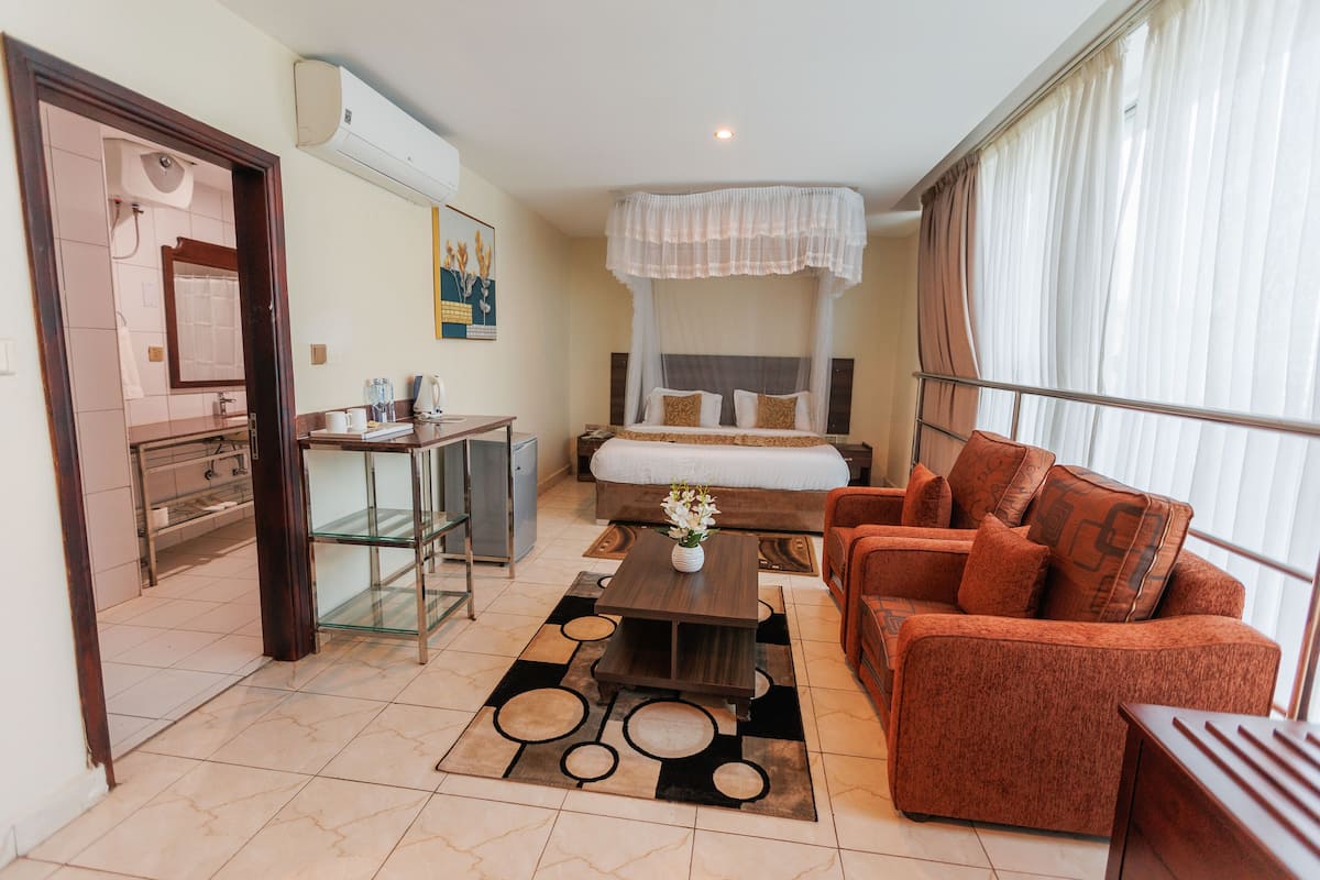 Una habitación de hotel con cama, sofá, escritorio, espejo y ventana con cortinas.