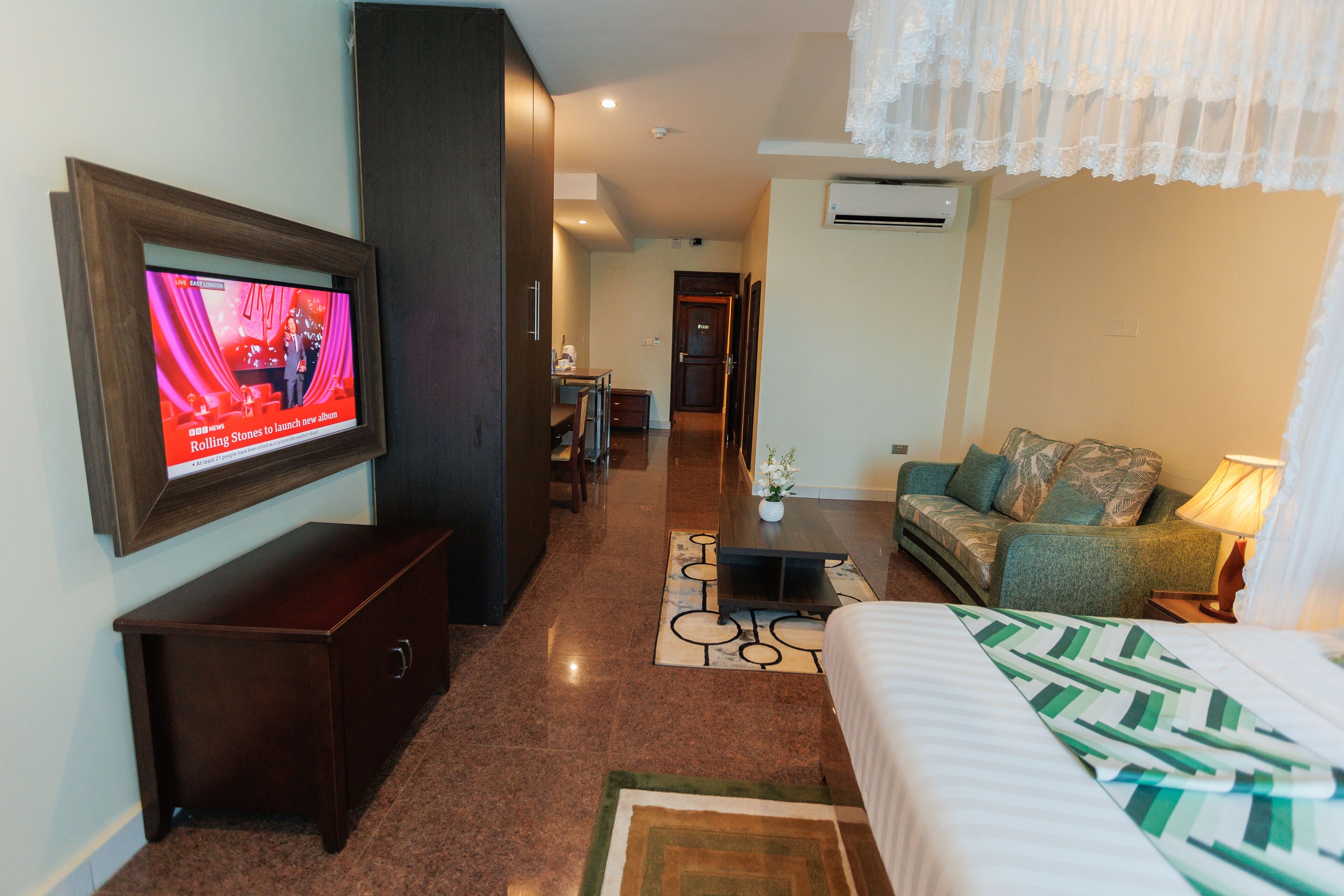A hotel room with a bed, a TV mounted on the wall, a sofa, a small table, and a desk.