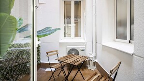 Un espacio exterior pequeño y resguardado con una mesa y sillas de madera, un ventilador y una ventana.