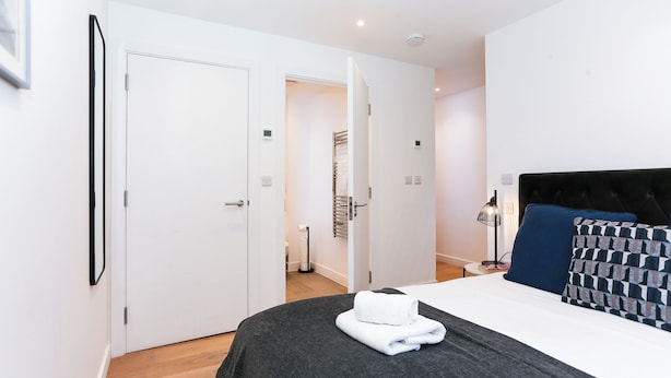 A modern hotel room with a neatly made bed, a black headboard, and a view into the bathroom. - Chapel - Central Studio Apartment (Bath)