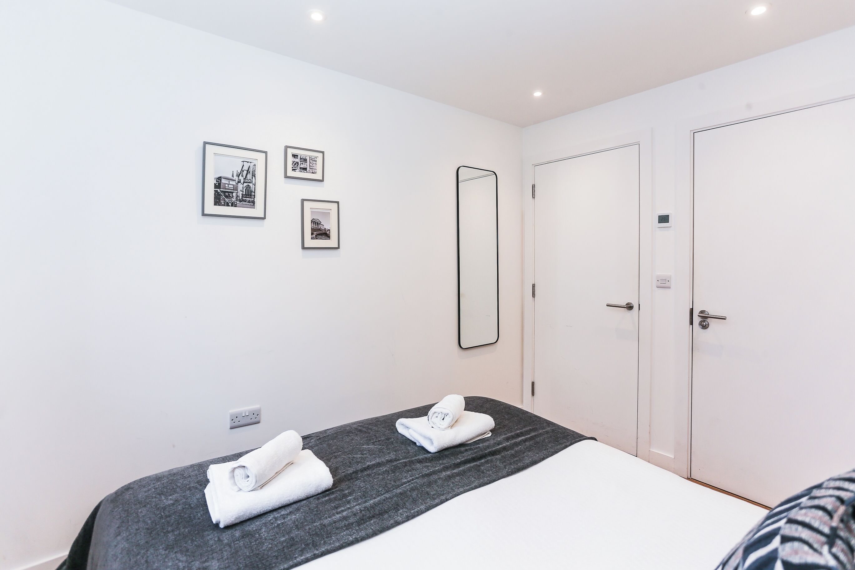 A hotel room with a bed, two towels, a large mirror, and three framed pictures on the wall.