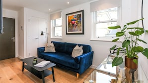 A modern living room with a blue sofa, a black coffee table, and a glass table with a plant. - Chapel - Central Studio Apartment (Bath)