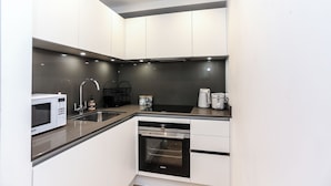 A modern kitchen with white cabinets, a stainless steel sink, a microwave, a dishwasher, and a coffee maker. - Chapel - Central Studio Apartment (Bath)