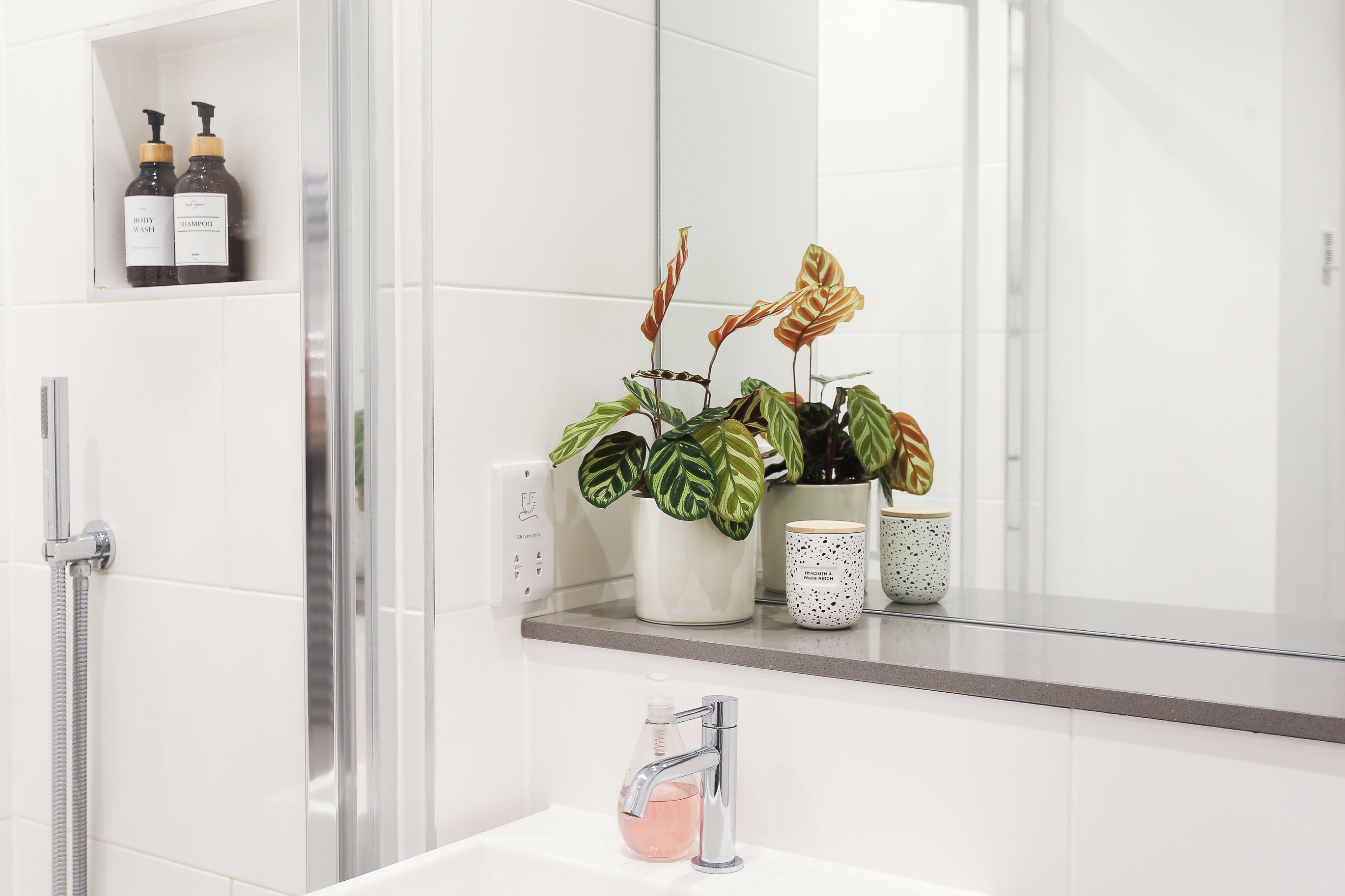 Un baño con ducha, lavamanos y dos botellas de champú en un estante.