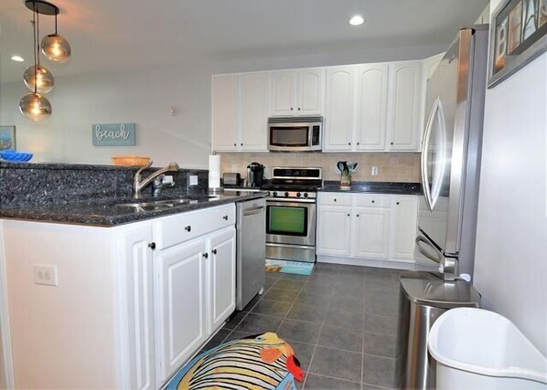A modern kitchen with white cabinets, stainless steel appliances, and a granite countertop. - BUDGET & DOG FRIENDLY! 2 BR, 2 BA- Pool/Tennis-Grande at Canal Point-Rehoboth (Rehoboth Beach)