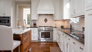A modern kitchen with white cabinetry, a central island, stainless steel appliances, and a wooden floor. - MINNeSTAY* Dean Parkway Estate Luxury | Spacious (Minneapolis)