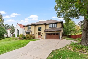 A two-story house with a garage, a driveway, and a well-maintained lawn. - MINNeSTAY* Dean Parkway Estate Luxury | Spacious (Minneapolis)