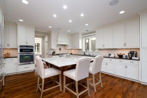 Una cocina moderna con armarios blancos, una isla central con sillas y electrodomésticos integrados.