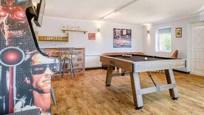 A pool table in a room with wooden flooring, a bar area with shelves, and a poster on the wall. - Luxury 5-bed House With Tennis Court & Games Room (Steyning)